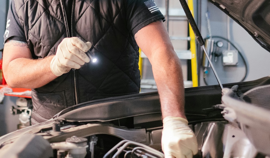 Car mechanic inspecting an engine with a flashlight for fleet servicing